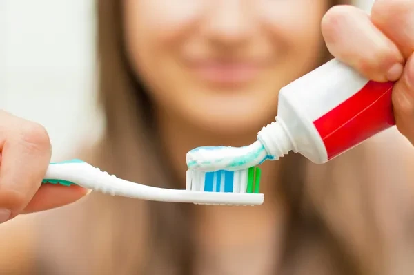 mujer sosteniendo cepillo y pasta dental