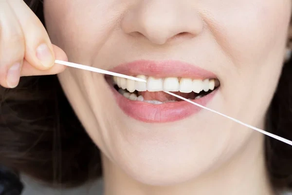 Mujer limpiándose los dientes con hilo dental